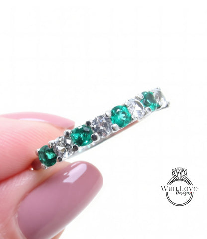 A close-up image of a person's hand holding a ring with a row of green and white gemstones.
