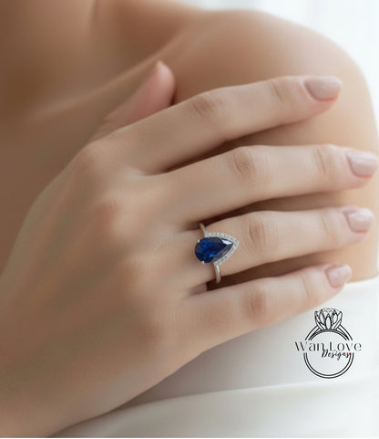 A close-up of a person's hand wearing a ring with a blue gemstone, resting on a white surface.
