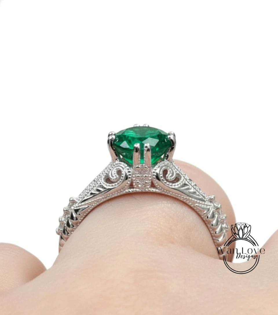 A close-up view of a silver engagement ring with a large, green gemstone set in an ornate, decorative band.