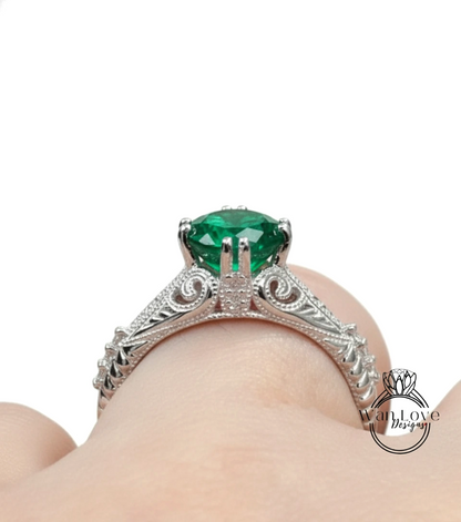 A close-up view of a silver engagement ring with a large, green gemstone set in an ornate, decorative band.