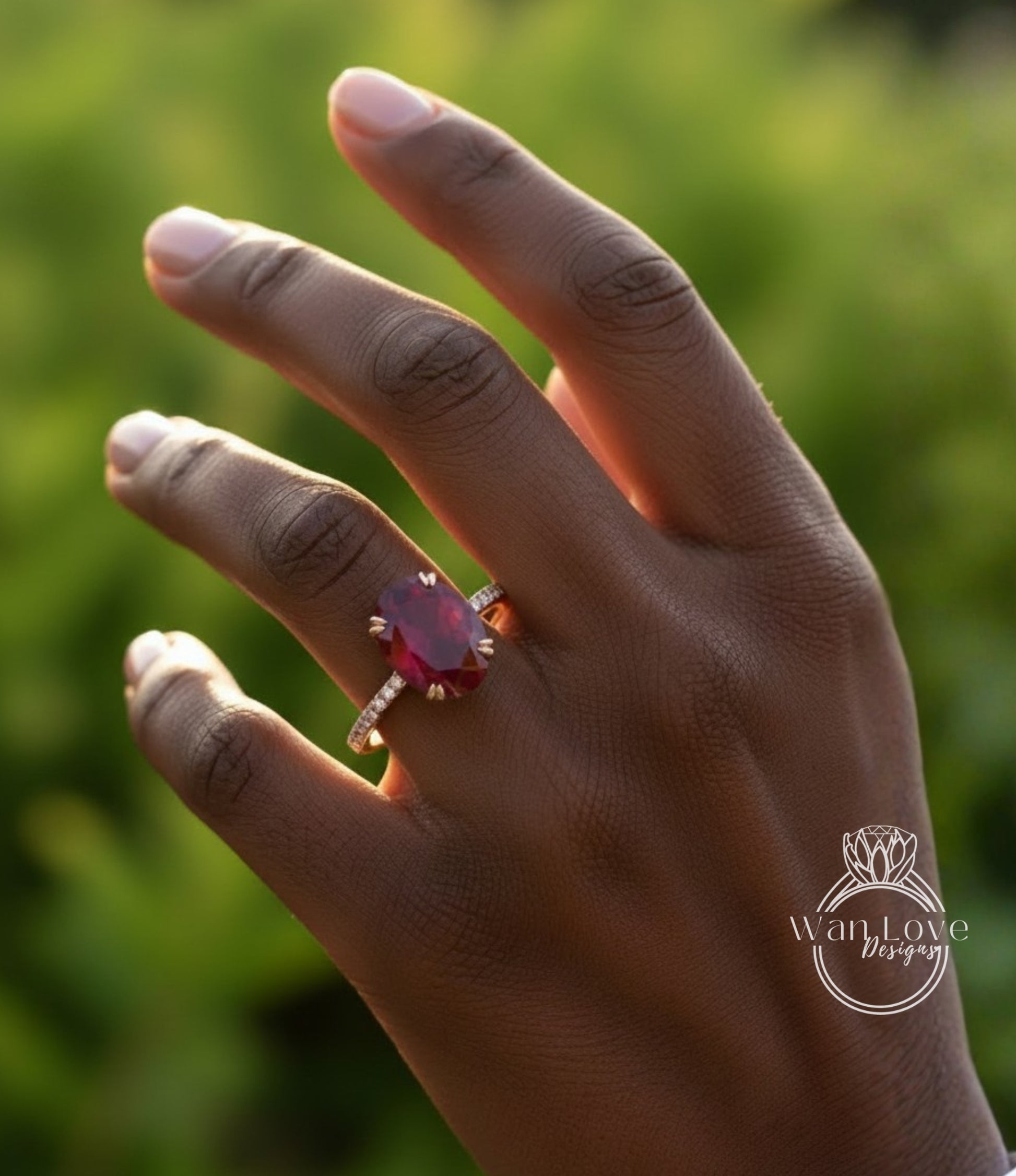 A close-up of a hand wearing a large, red gemstone ring against a blurred green background.