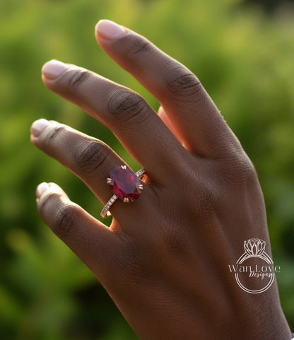 A close-up of a hand wearing a large, red gemstone ring against a blurred green background.