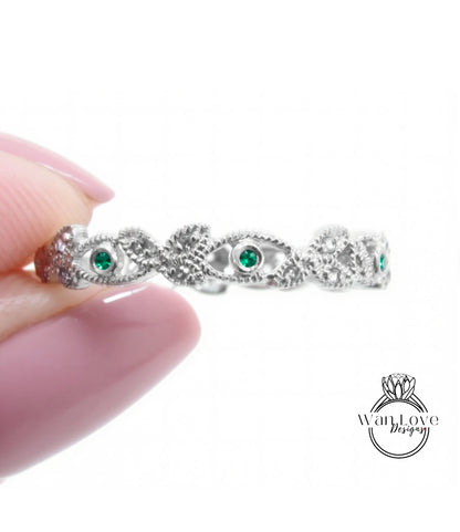 A hand holding a silver ring with green gemstones.