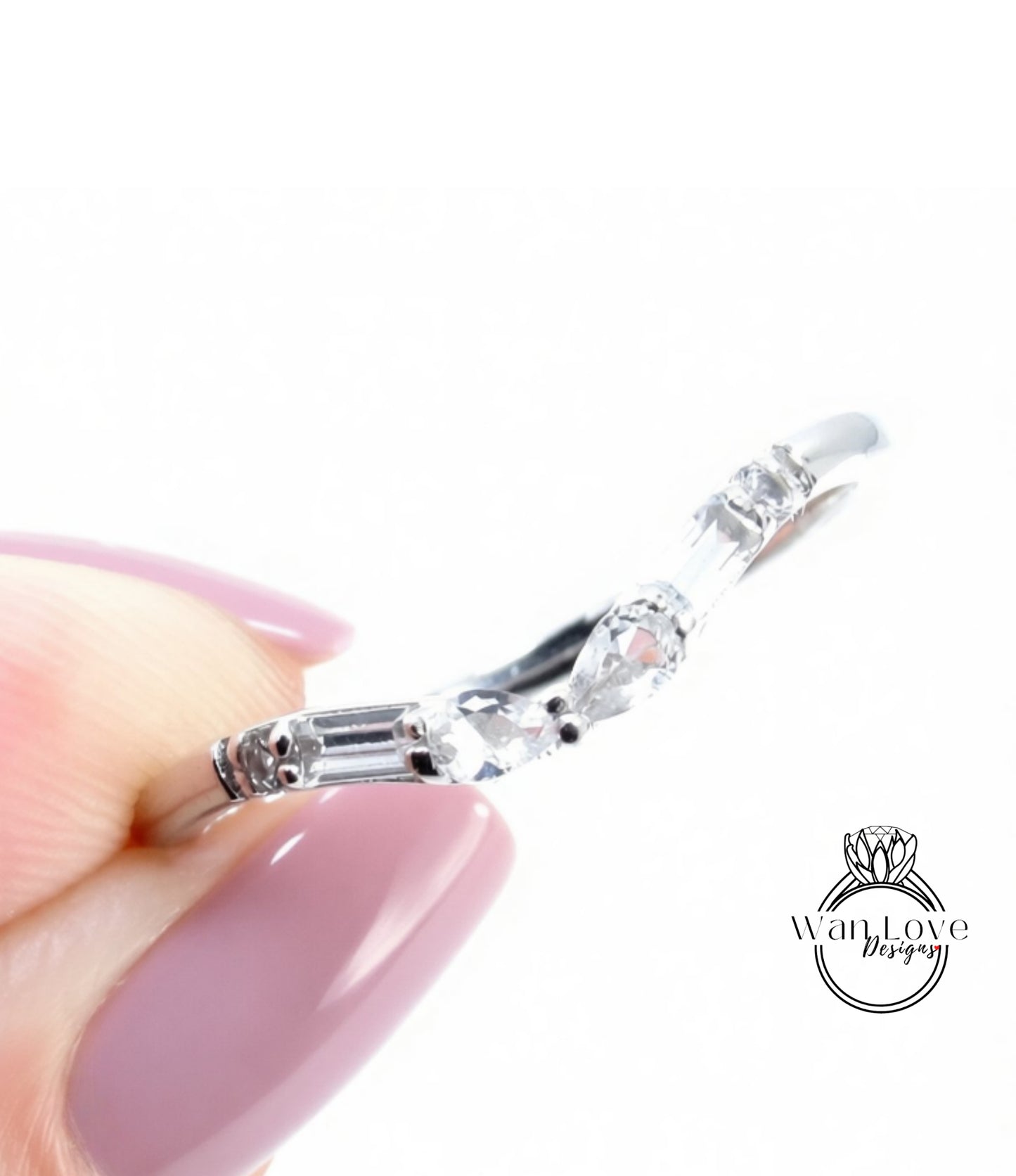 A close-up of a person's hand holding a silver ring with a clear gemstone.
