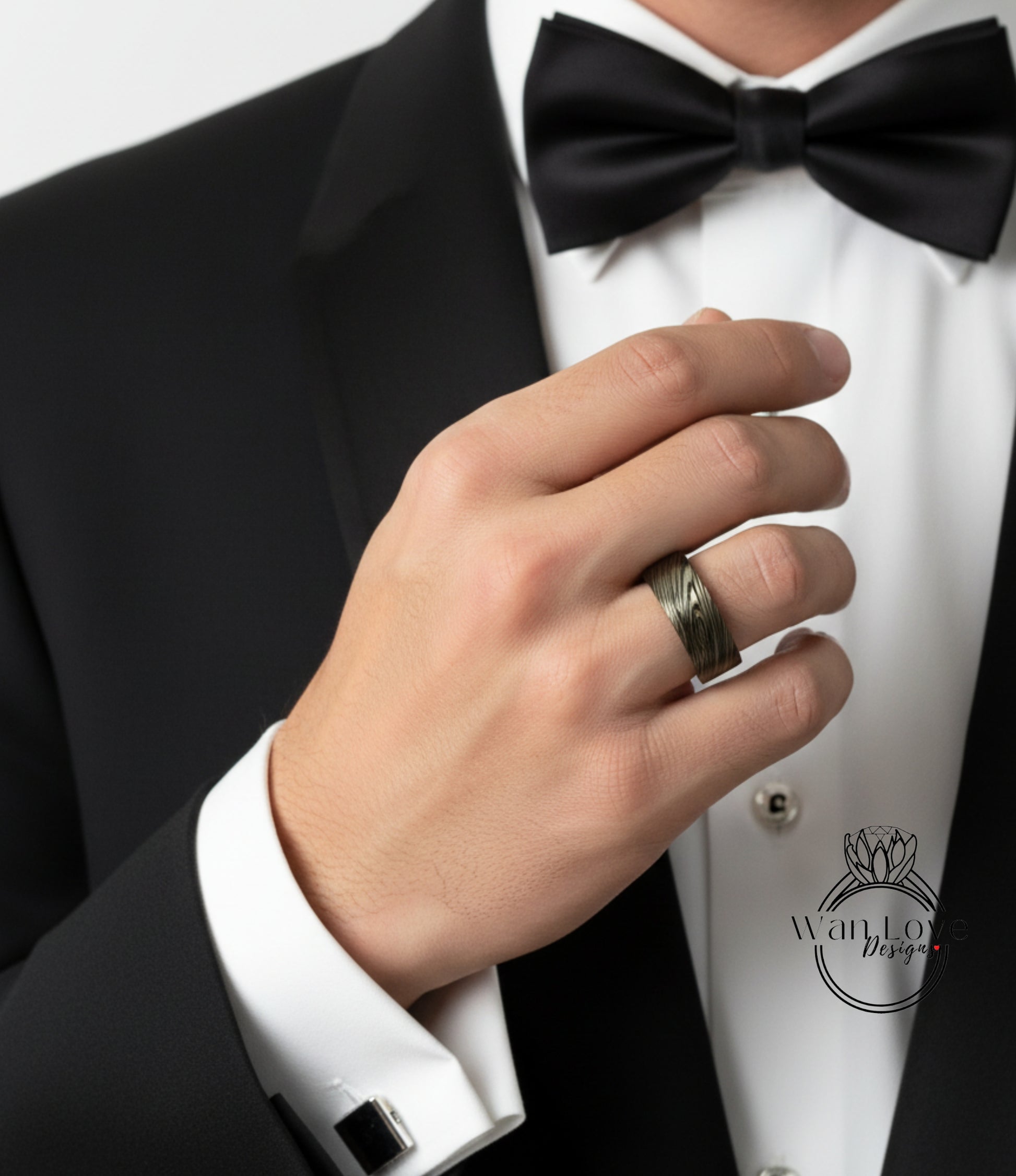 A close-up of a man's hand wearing a black suit and bow tie, with a ring on his finger.
