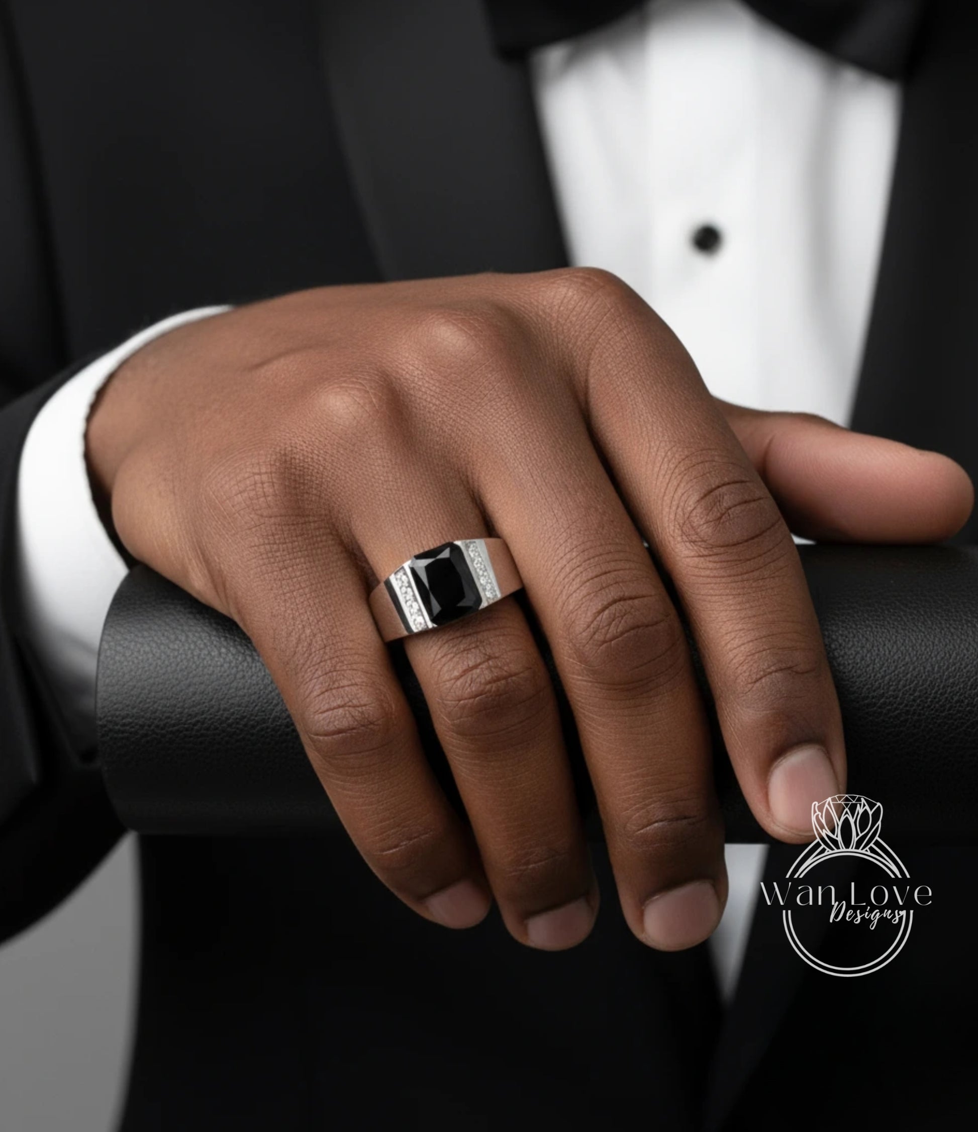 A close-up of a person's hand wearing a ring, with a tuxedo jacket visible in the background.