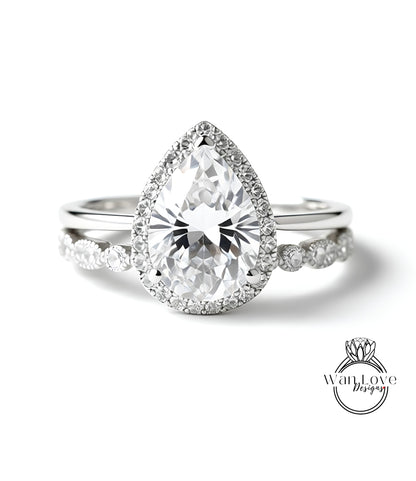 A close-up of a diamond engagement ring with a large pear-shaped diamond set in a halo of smaller diamonds, surrounded by a band of smaller diamonds.