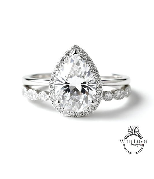 A close-up of a diamond engagement ring with a large pear-shaped diamond set in a halo of smaller diamonds, surrounded by a band of smaller diamonds.