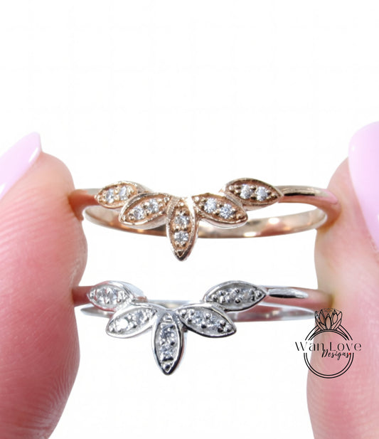 A close-up image of a person's fingers holding two rings with leaf-shaped designs and small diamonds.