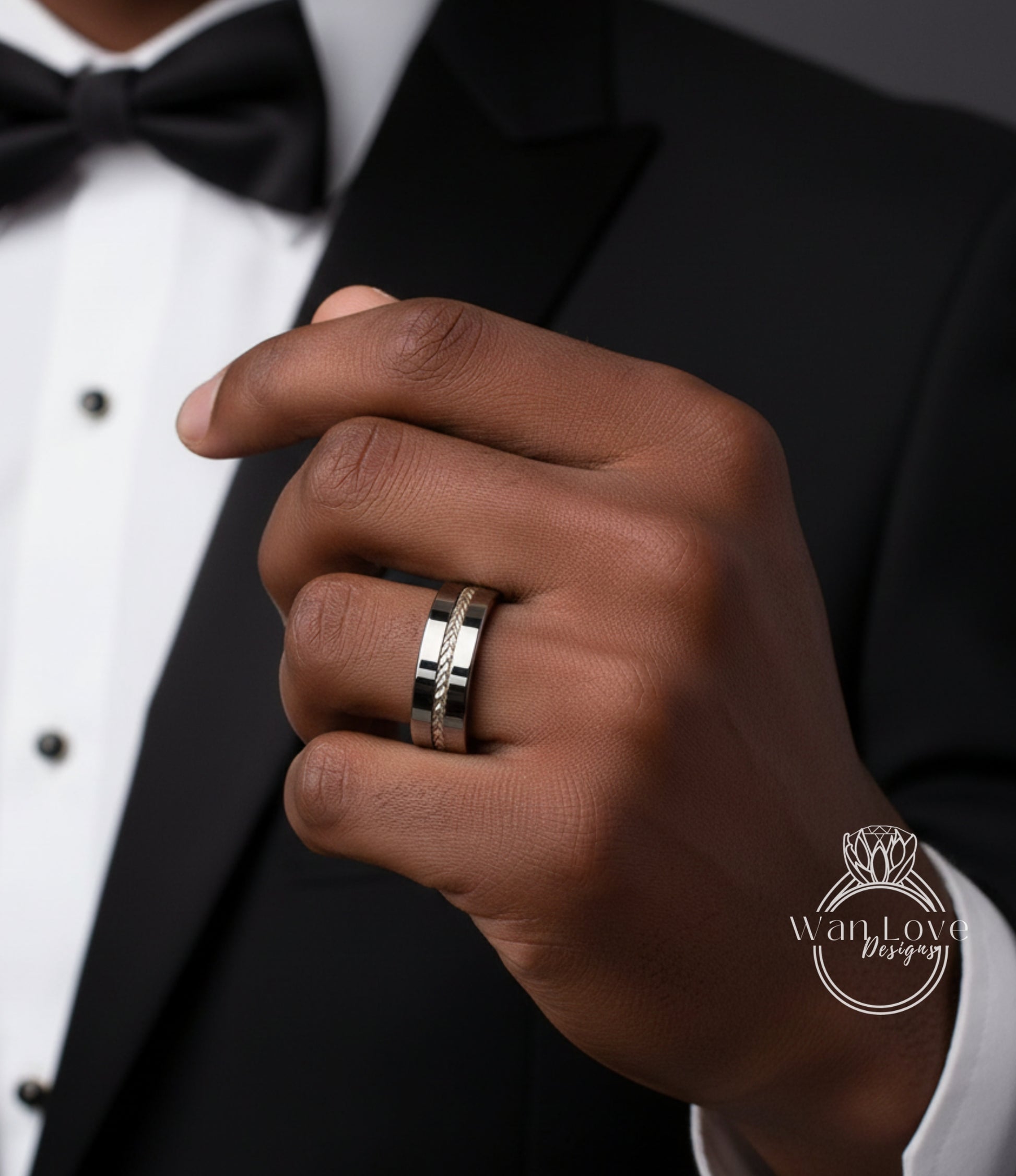 A close-up of a person's hand wearing a silver wedding ring, with a black tuxedo jacket visible in the background.