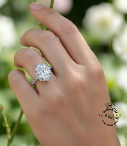 A close-up of a hand wearing a diamond engagement ring, with a blurred background of greenery.
