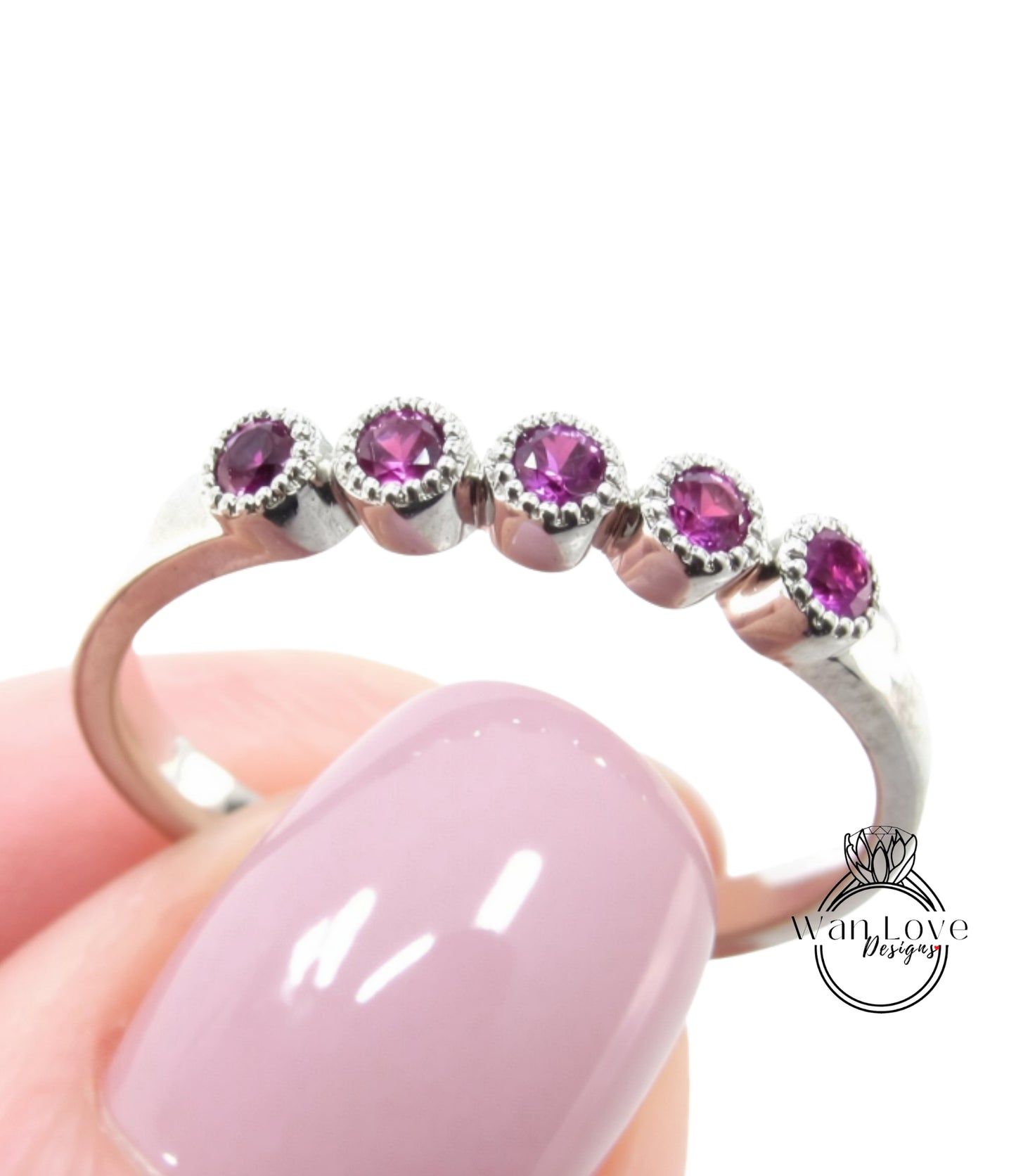 A close-up of a person's hand holding a ring with a row of purple gemstones on the ring band.
