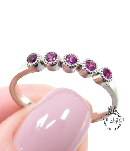 A close-up of a person's hand holding a ring with a row of purple gemstones on the ring band.