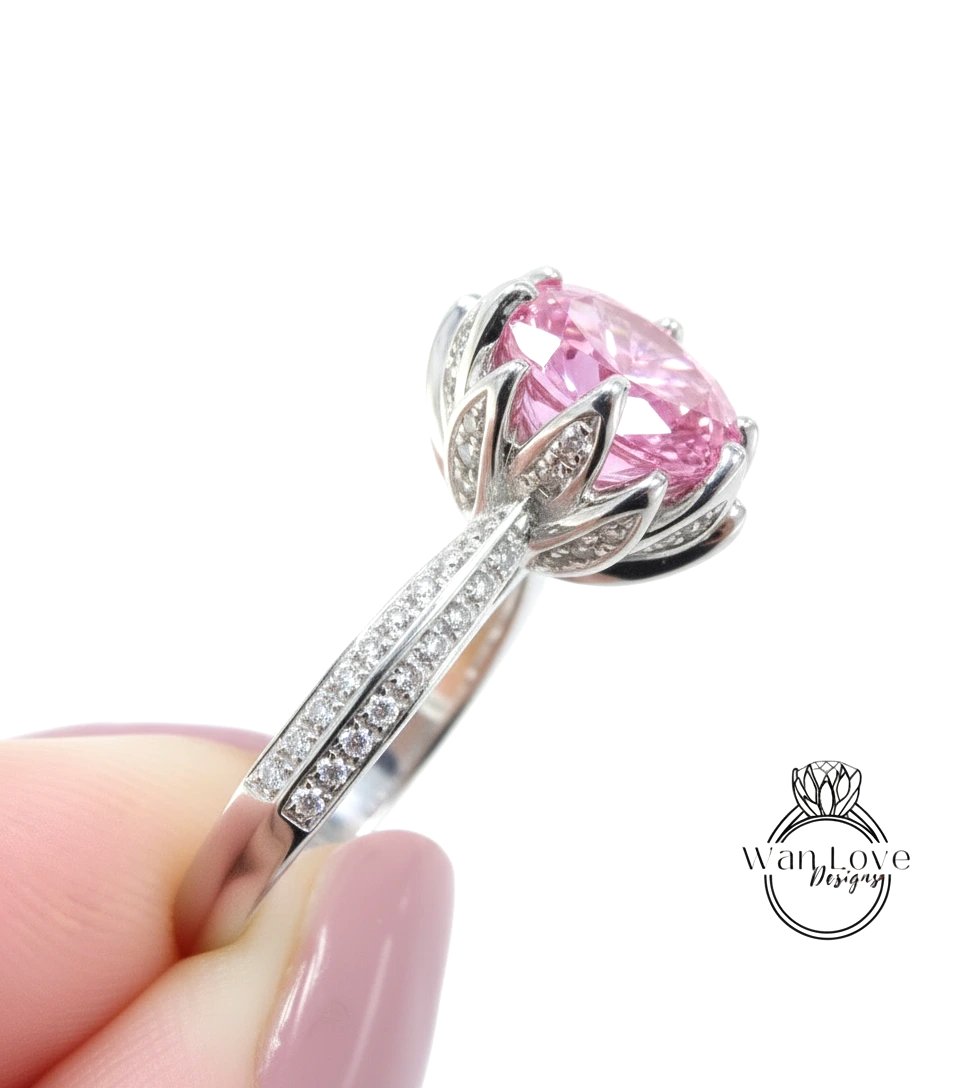A close-up of a person's hand holding a silver ring with a large pink gemstone, likely a diamond.