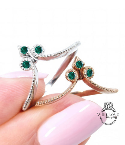 A close-up image of a person's hand holding a ring with a floral design and green gemstones.