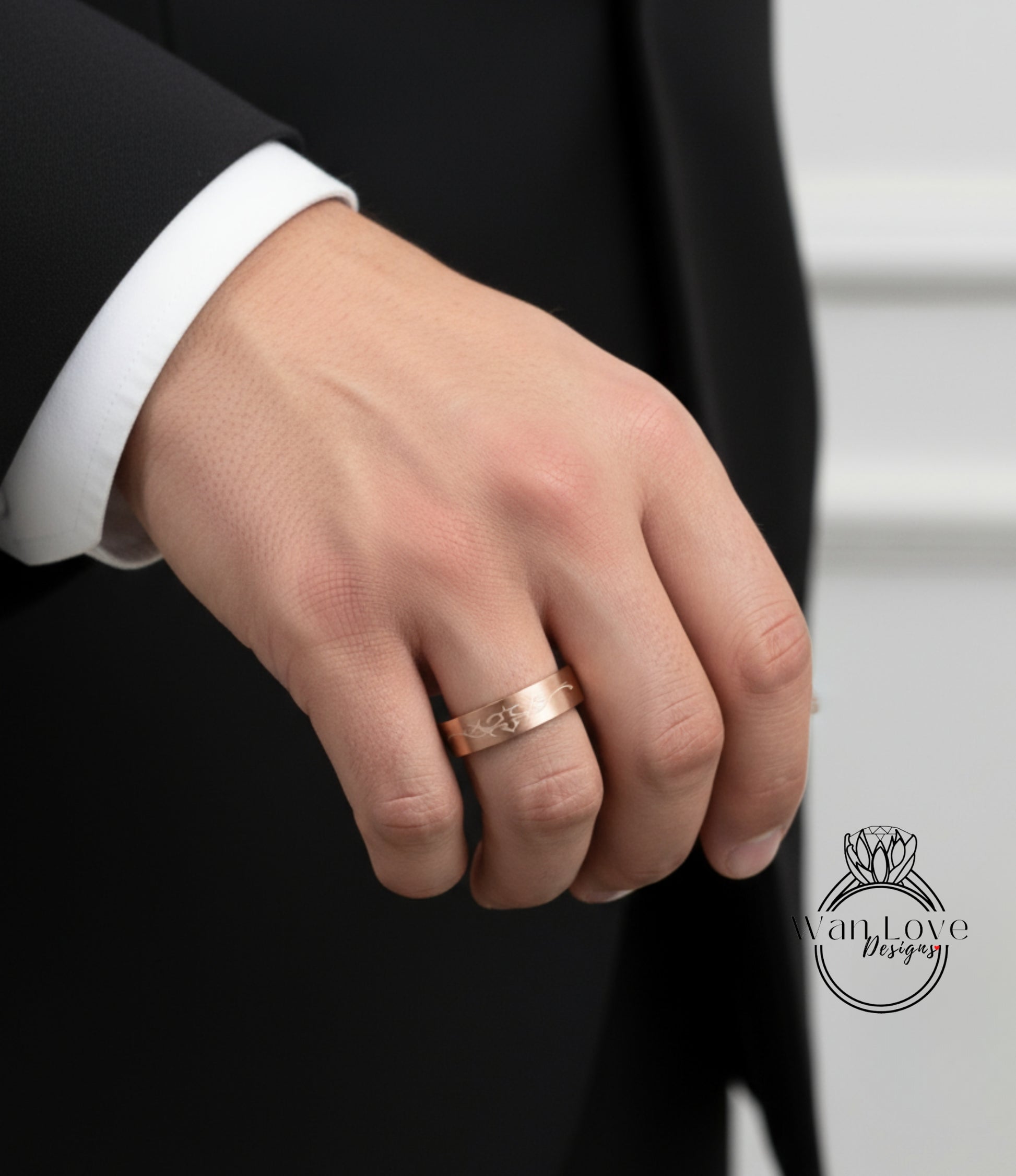 A close-up of a person's hand wearing a gold ring, with a black suit jacket visible in the background.