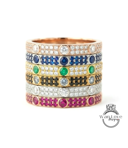A stack of rings with various colored gemstones and diamonds set in a gold band.
