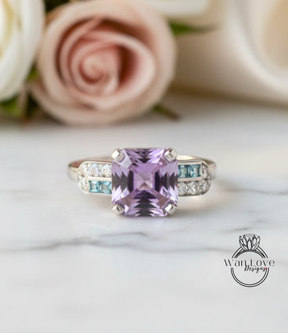 A ring with a large purple gemstone, surrounded by smaller blue gemstones, sits on a marble surface.