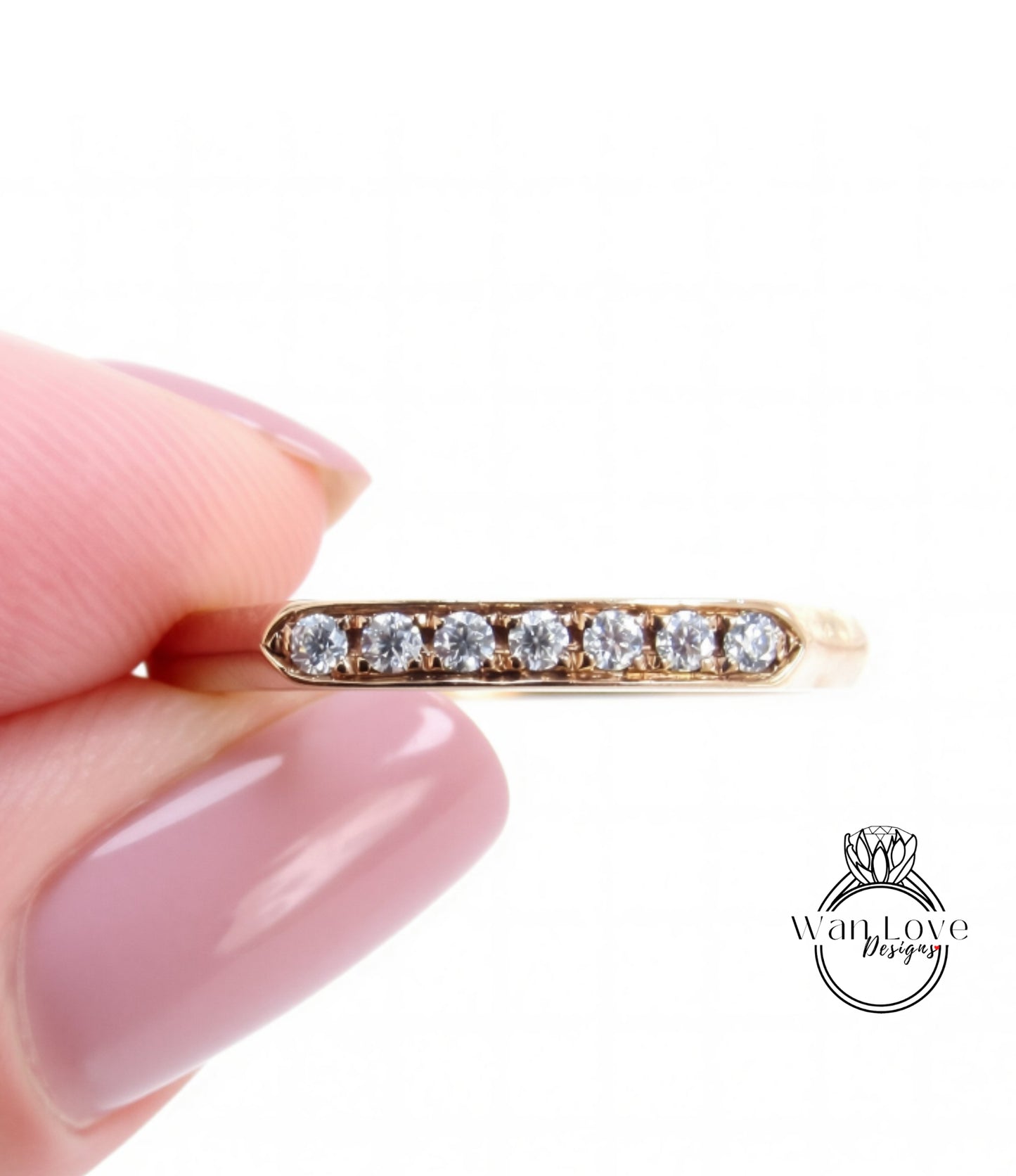 A close-up image of a person's hand holding a gold ring with a row of small diamonds set in it.