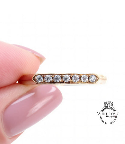 A close-up image of a person's hand holding a gold ring with a row of small diamonds set in it.