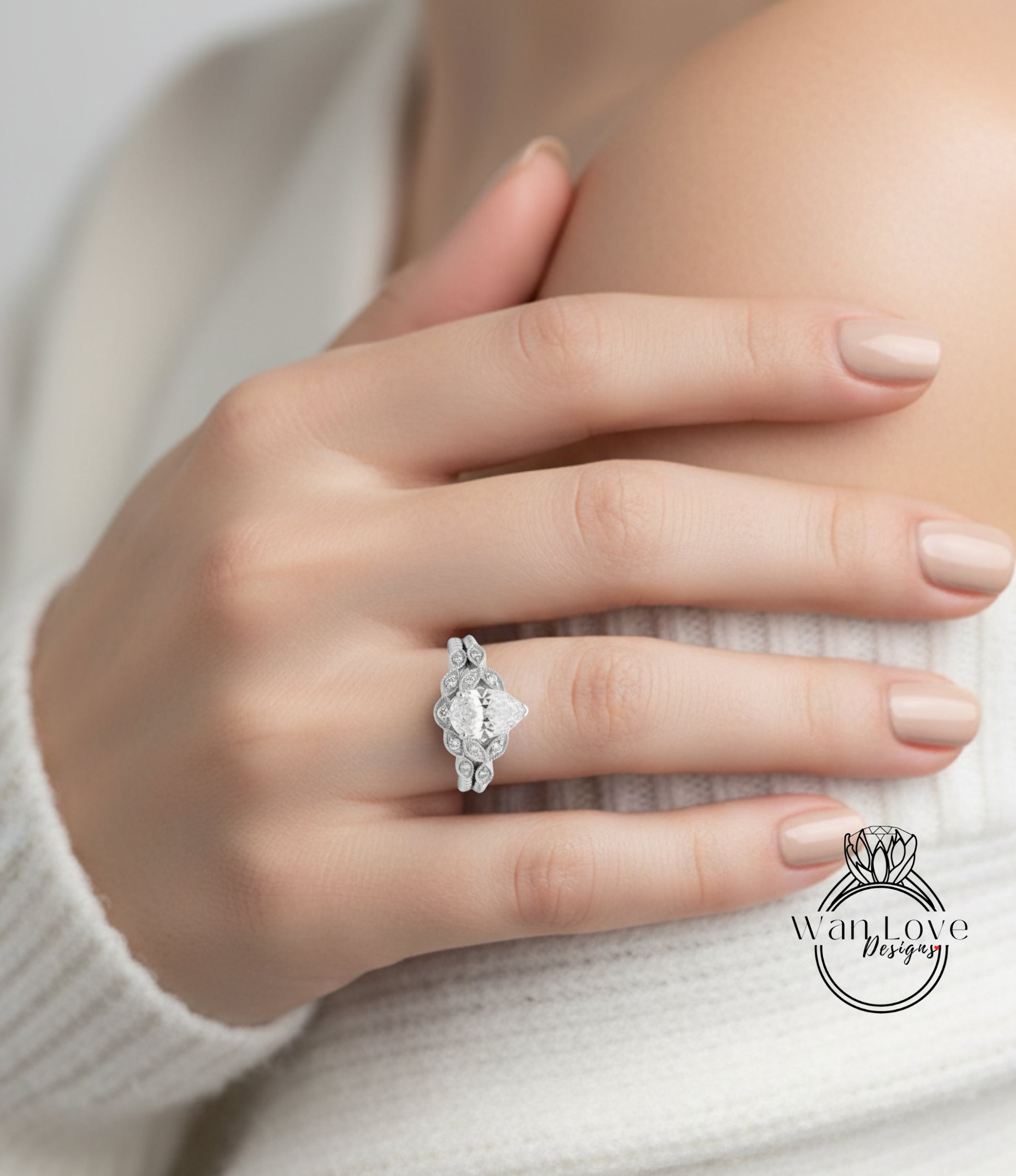 A close-up of a person's hand wearing a diamond engagement ring, with a white sweater visible in the background.