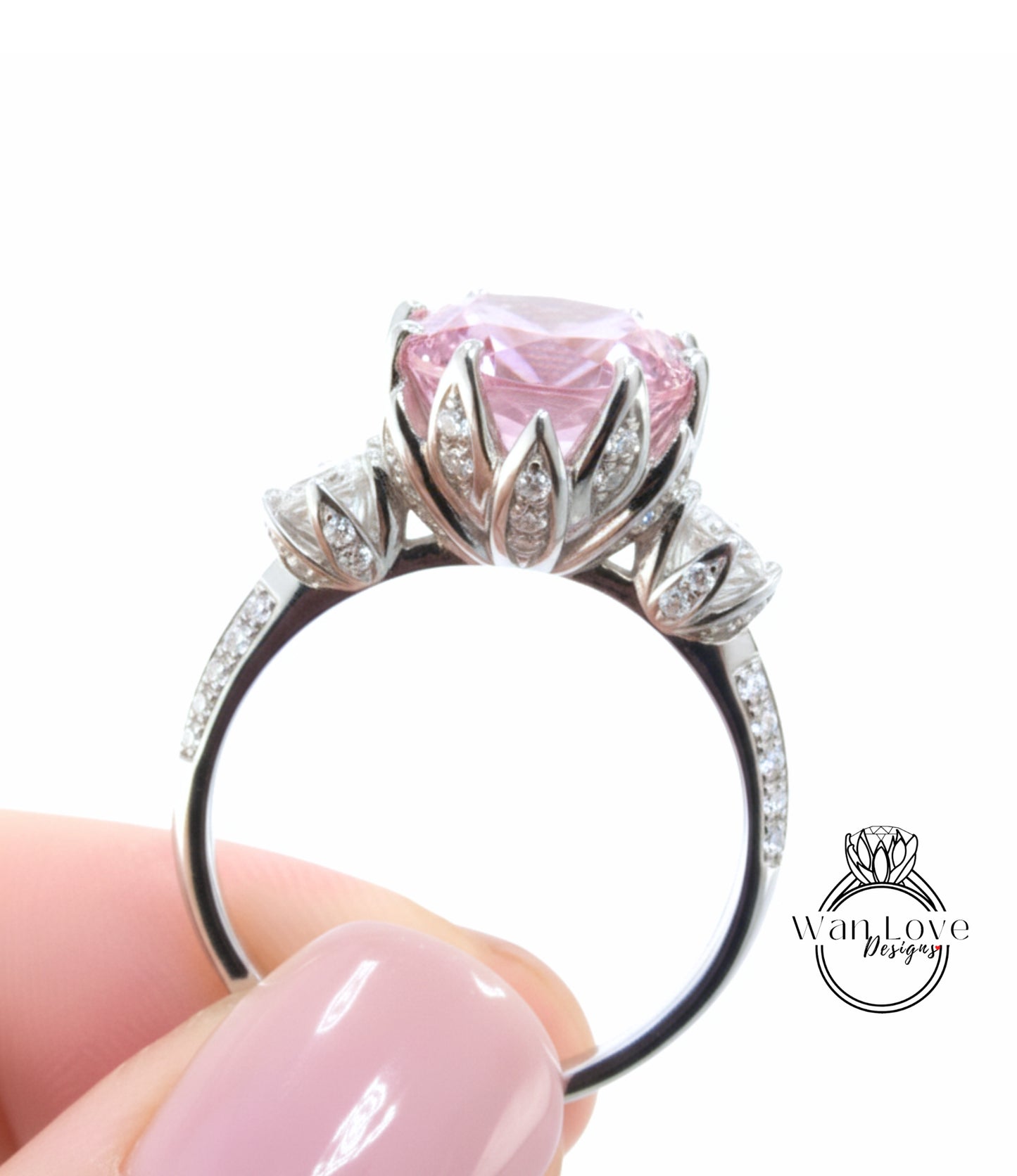 A close-up image of a person's hand holding a silver ring with a large pink gemstone, likely a diamond, on the ring.