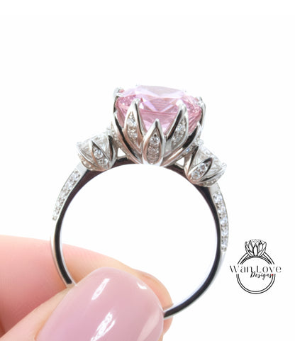 A close-up image of a person's hand holding a silver ring with a large pink gemstone, likely a diamond, on the ring.