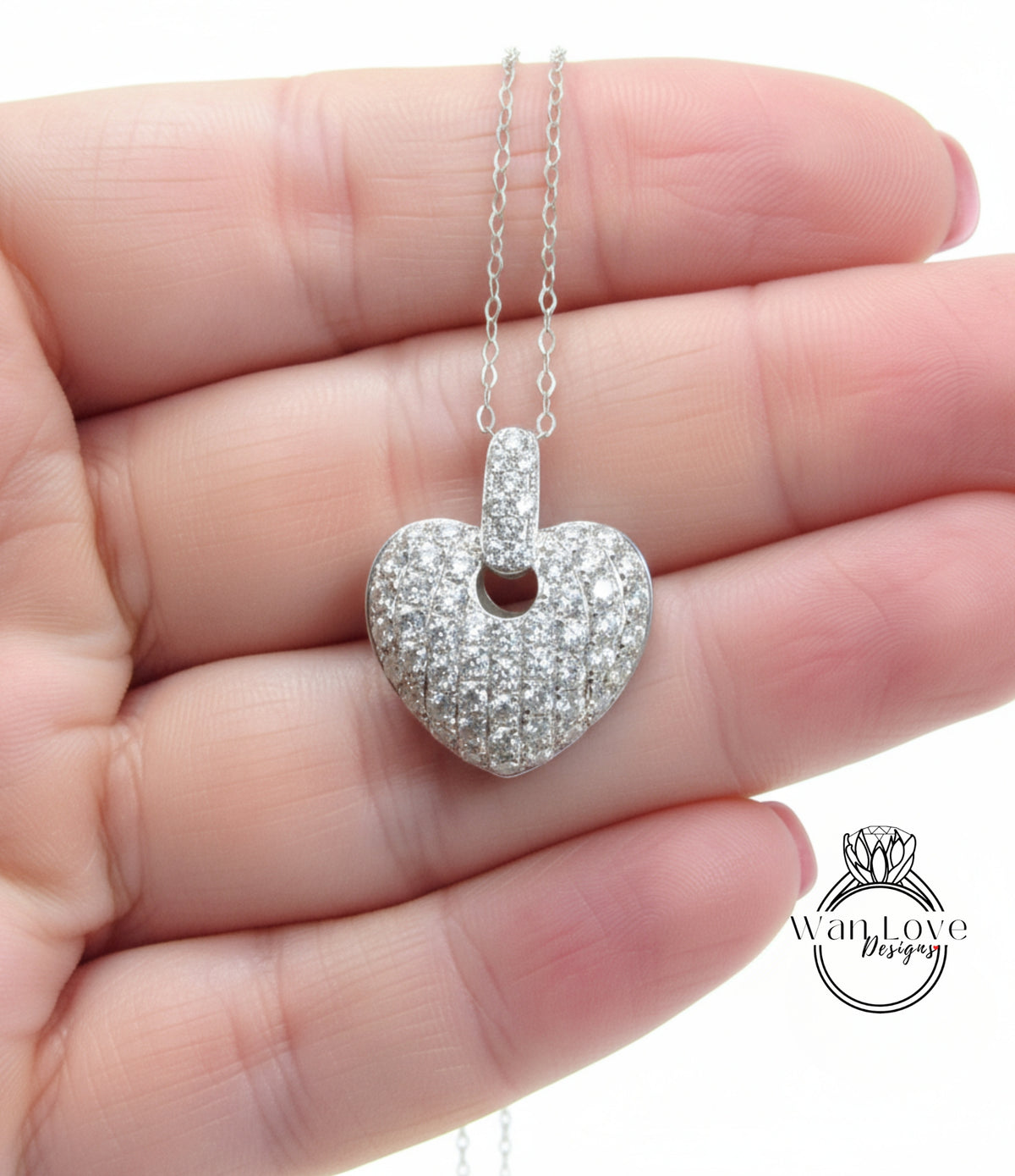A hand holding a delicate silver necklace with a heart-shaped pendant adorned with sparkling diamonds.