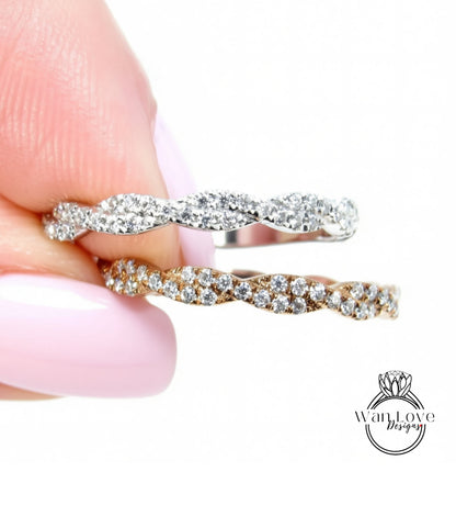 A close-up of a person's hand holding a ring with a twisted band and sparkling diamonds.