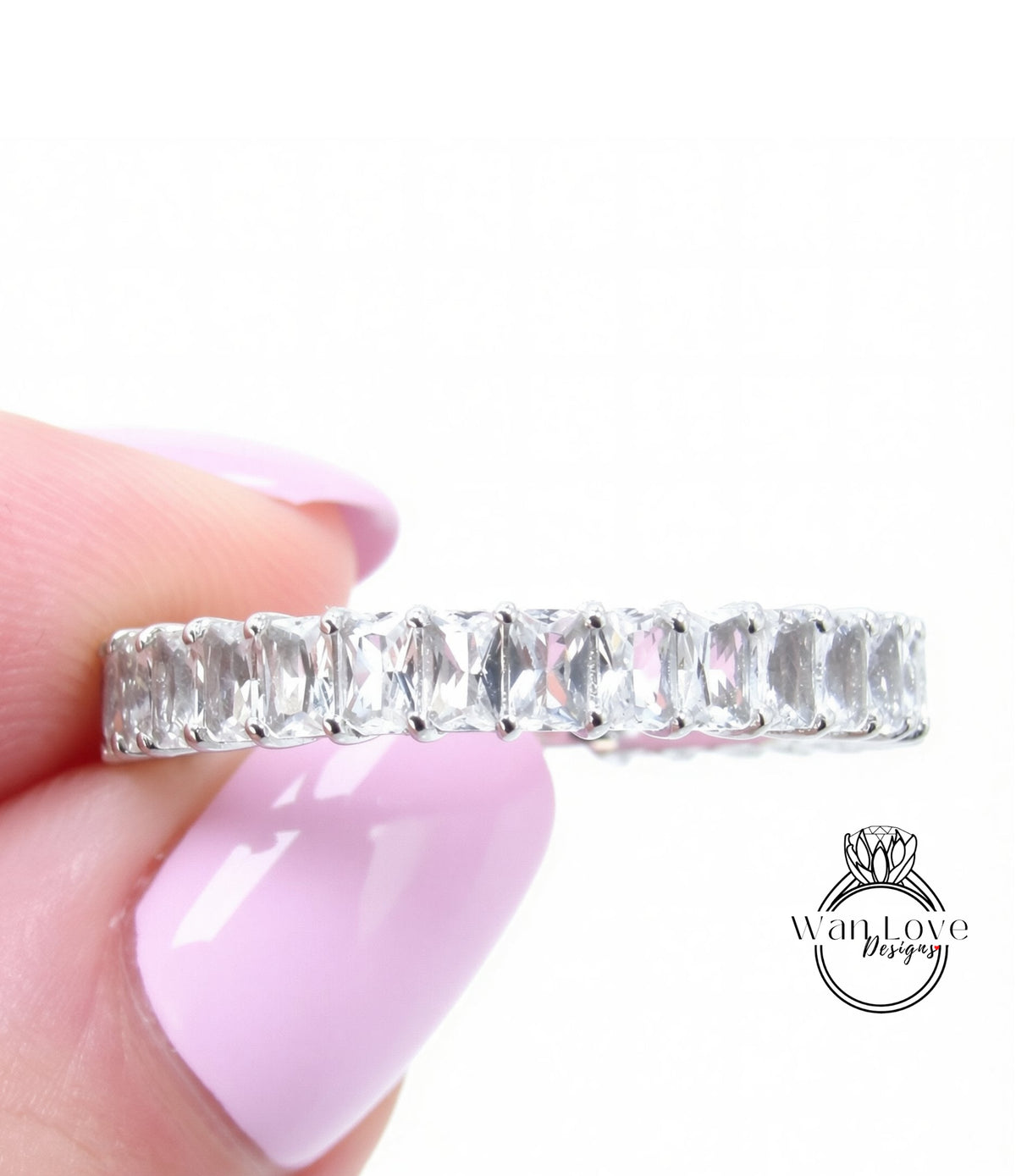 A close-up image of a person's hand holding a ring with a row of clear gemstones.