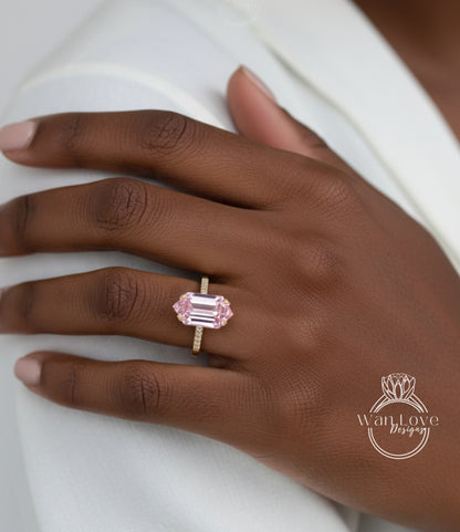 A close-up of a hand wearing a gold ring with a large pink gemstone, resting on a white surface.