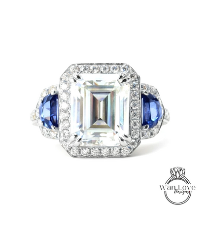 A stunning diamond engagement ring with a large central diamond surrounded by smaller diamonds on either side, set in a halo of smaller diamonds. The ring is adorned with blue gemstones on either side of the central diamond, creating a striking contrast against the white background.