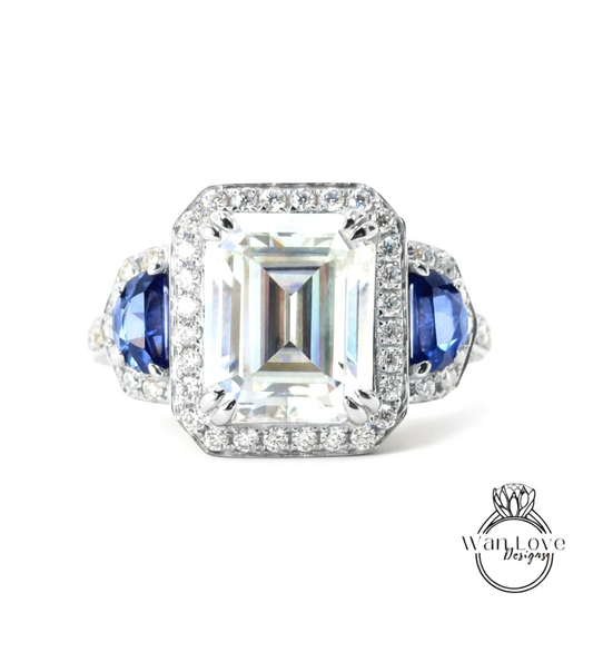 A stunning diamond engagement ring with a large central diamond surrounded by smaller diamonds on either side, set in a halo of smaller diamonds. The ring is adorned with blue gemstones on either side of the central diamond, creating a striking contrast against the white background.