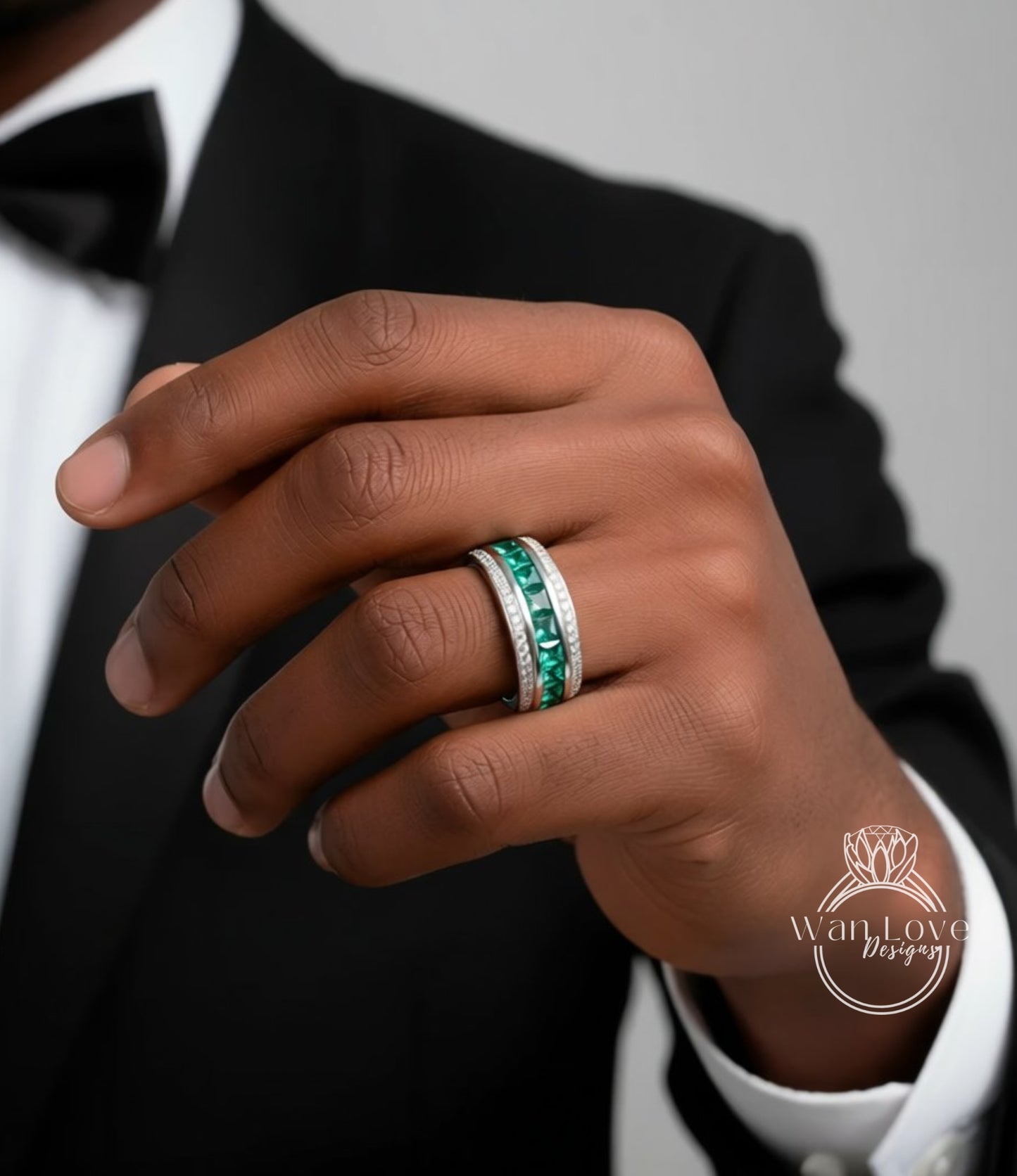 A close-up of a person's hand wearing a ring with a green gemstone, possibly an emerald, and a band of diamonds.