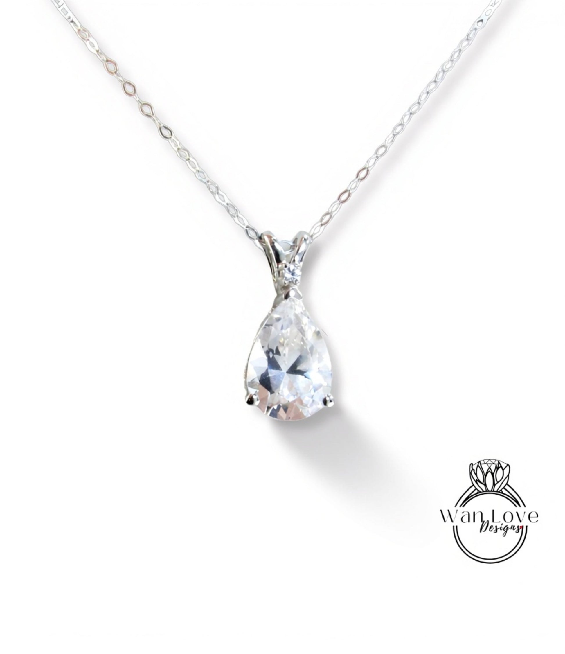A close-up view of a delicate silver necklace with a large, clear pear-shaped gemstone pendant.