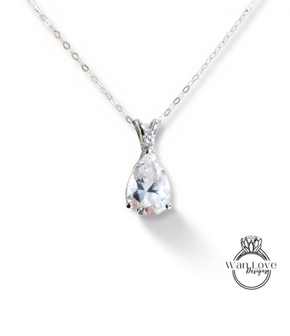 A close-up view of a delicate silver necklace with a large, clear pear-shaped gemstone pendant.