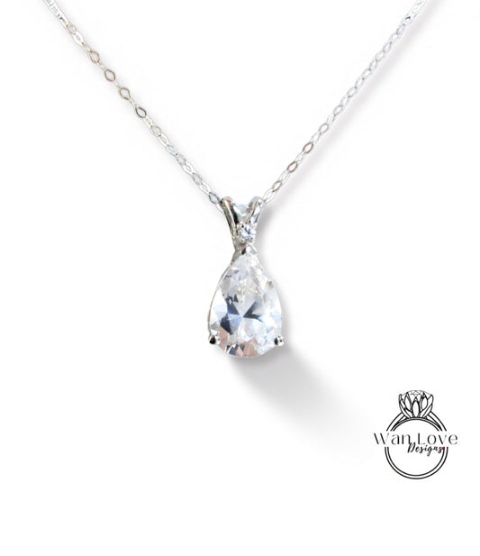 A close-up view of a delicate silver necklace with a large, clear pear-shaped gemstone pendant.