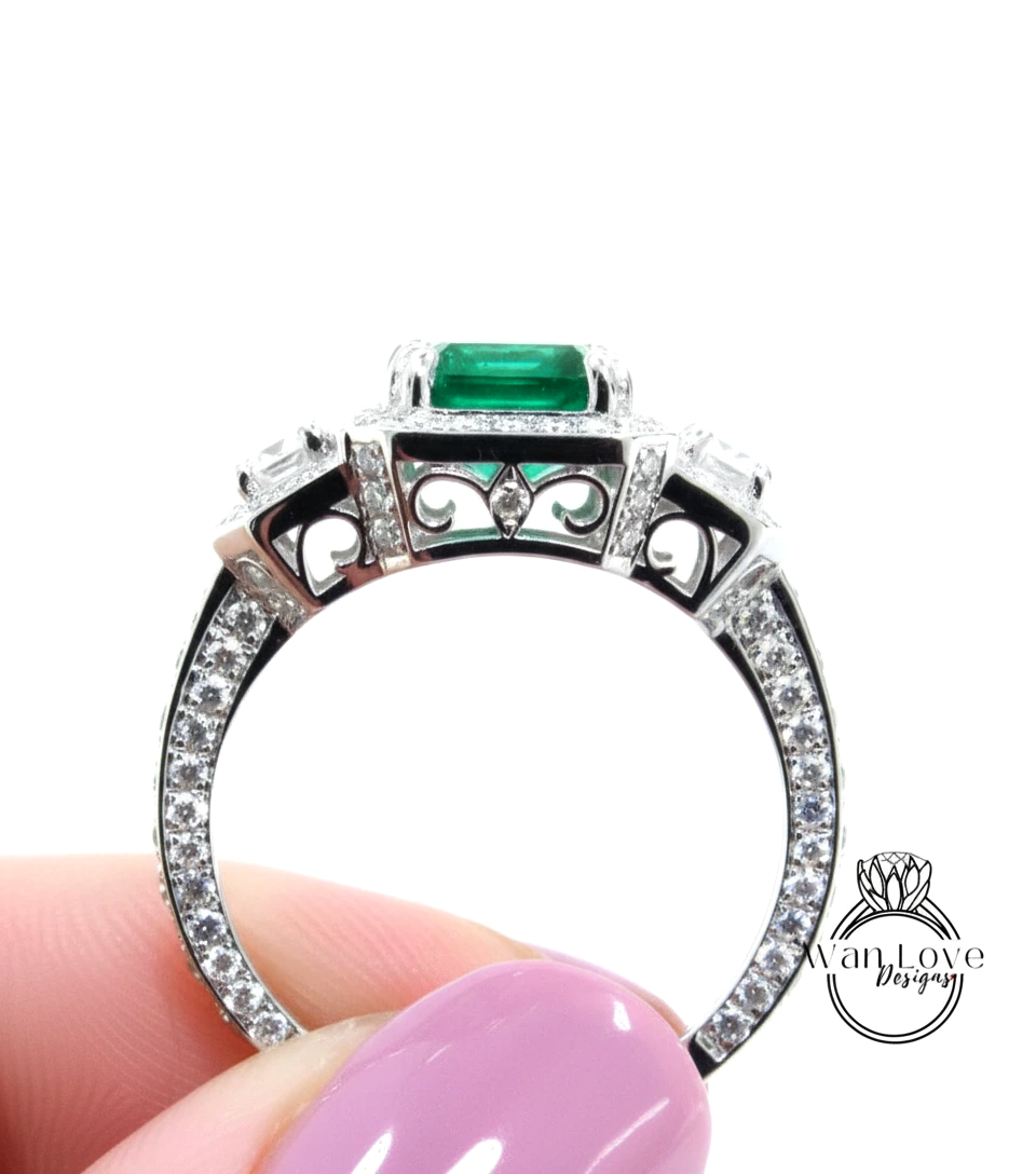 A close-up of a person's hand holding a ring with a large green gemstone and sparkling diamonds.