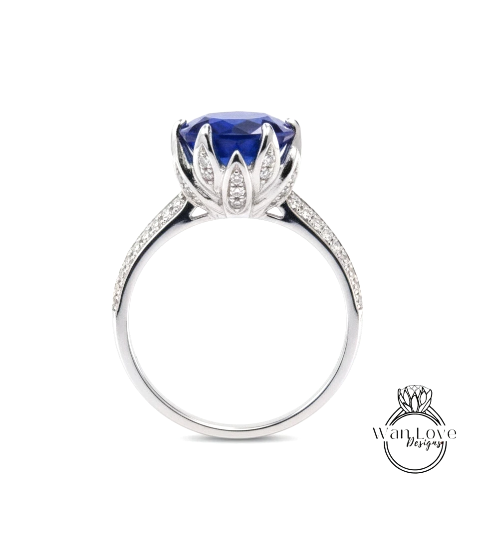 A silver ring with a large blue gemstone, likely a sapphire, at the center. The ring has a delicate flower-like design around the gemstone, and it is set in a silver band.