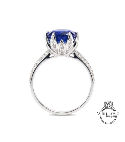 A silver ring with a large blue gemstone, likely a sapphire, at the center. The ring has a delicate flower-like design around the gemstone, and it is set in a silver band.