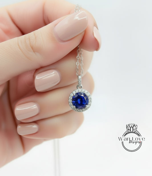 A hand holding a necklace with a blue gemstone pendant.