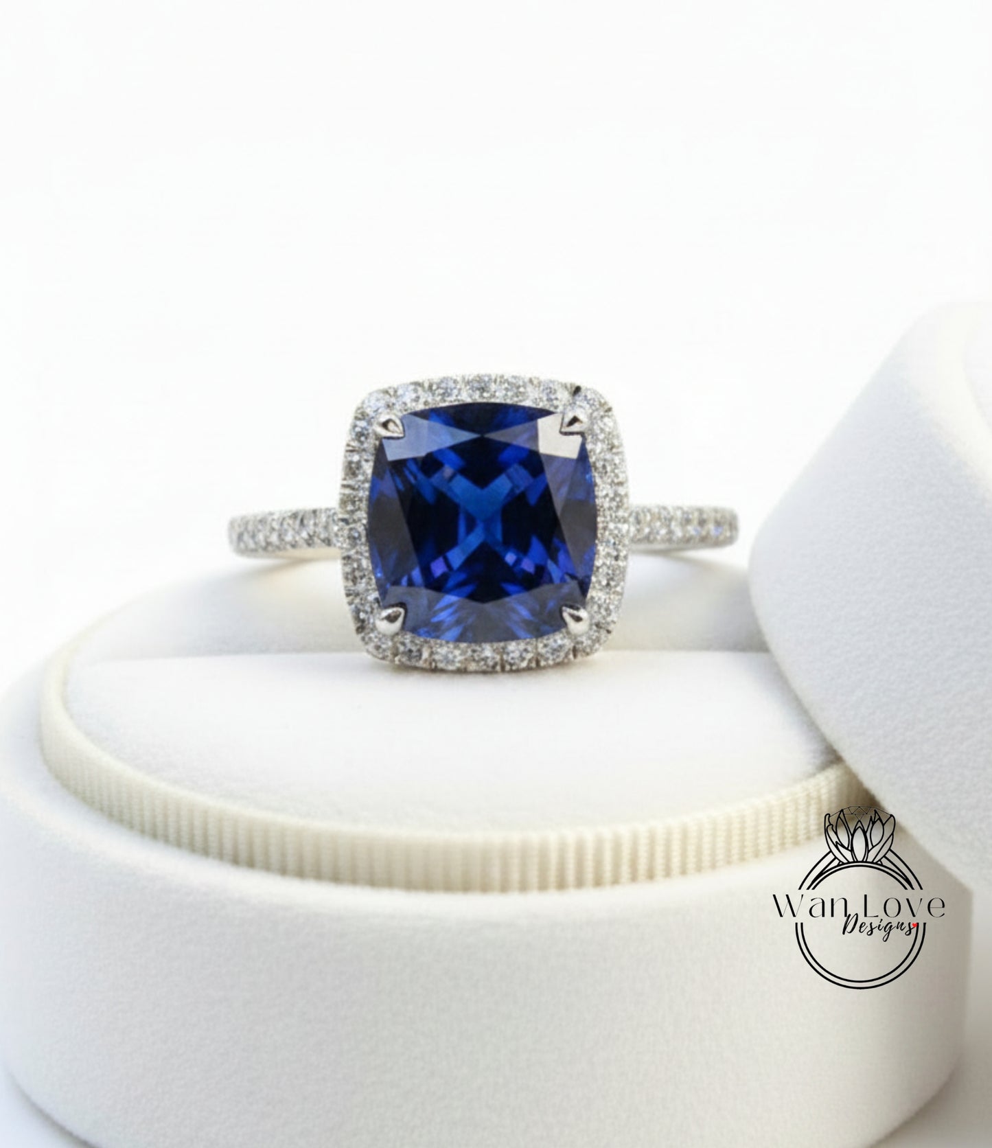 A stunning blue gemstone ring with a halo of diamonds, displayed on a white jewelry box.