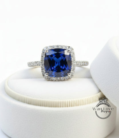 A stunning blue gemstone ring with a halo of diamonds, displayed on a white jewelry box.