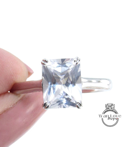 A close-up image of a person's hand holding a ring with a large, clear gemstone, likely a diamond.