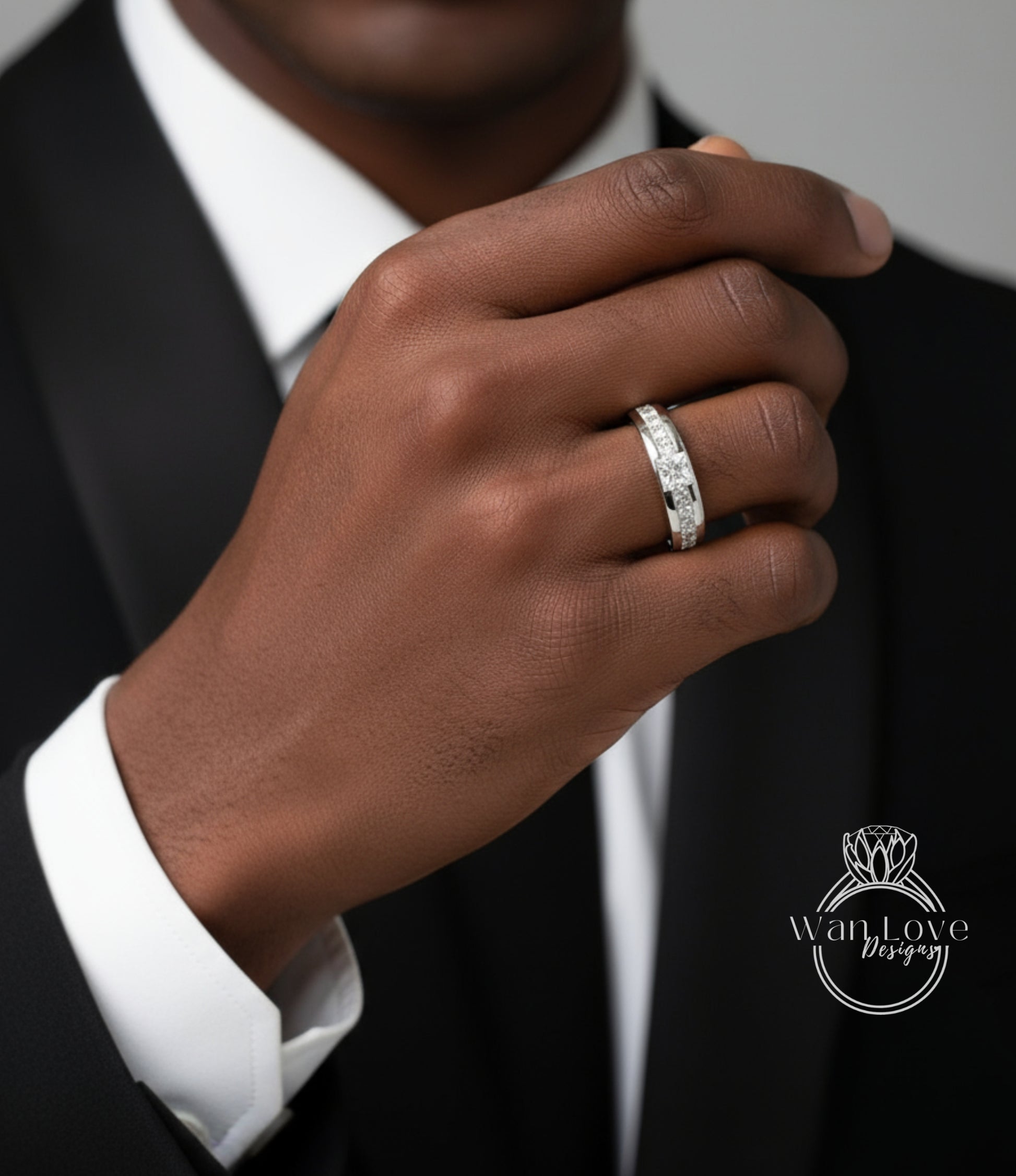 A close-up of a person's hand wearing a diamond ring, with a black suit jacket visible.