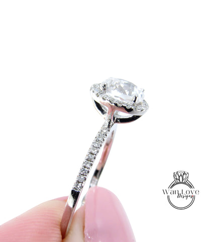 A close-up of a diamond engagement ring being held in a hand, with a focus on the center stone and the intricate details of the ring.