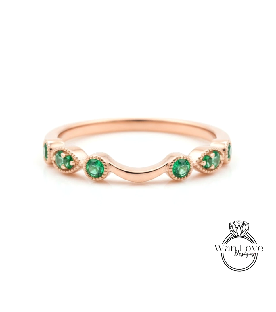 A rose gold ring with a curved band and a row of green gemstones, including emeralds, set in the center.