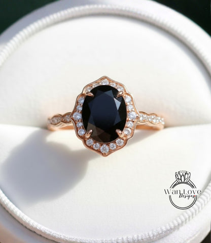A close-up image of a gold ring with a large oval-shaped black gemstone, surrounded by smaller diamonds, placed in a white jewelry box.