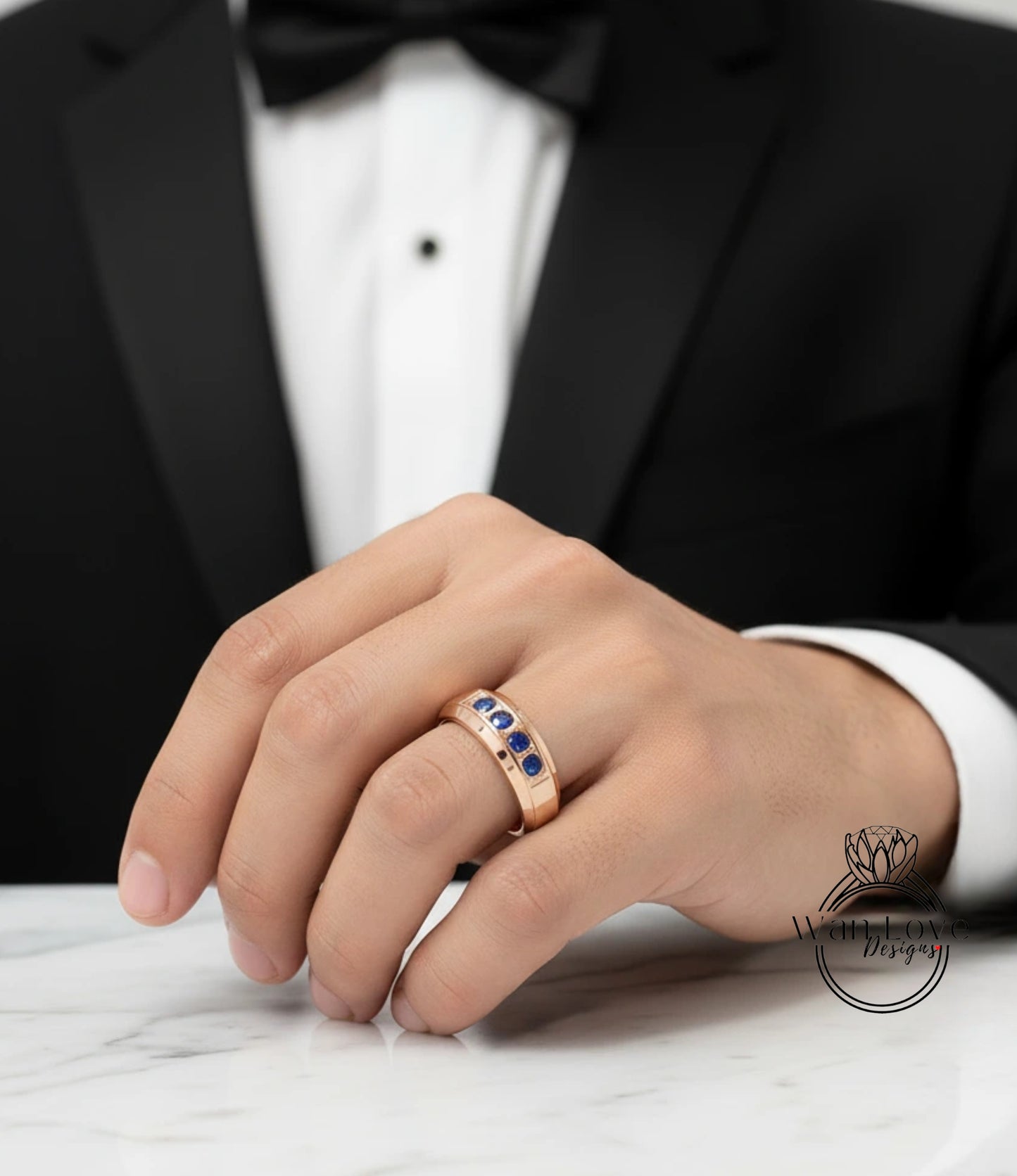 A close-up of a person's hand wearing a gold ring with blue gemstones, wearing a black tuxedo.