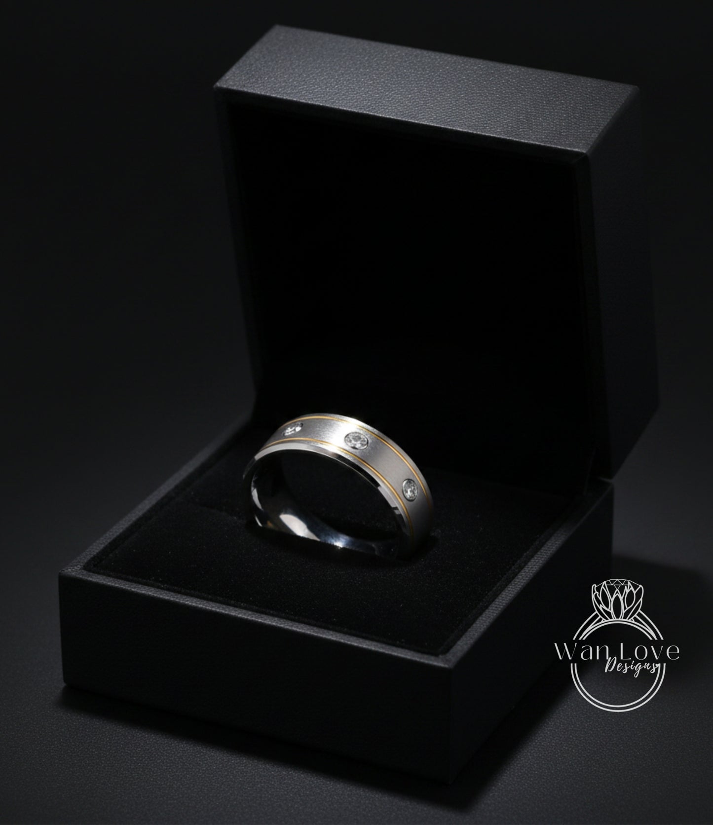 A silver ring with three diamonds is displayed in a black jewelry box against a dark background.